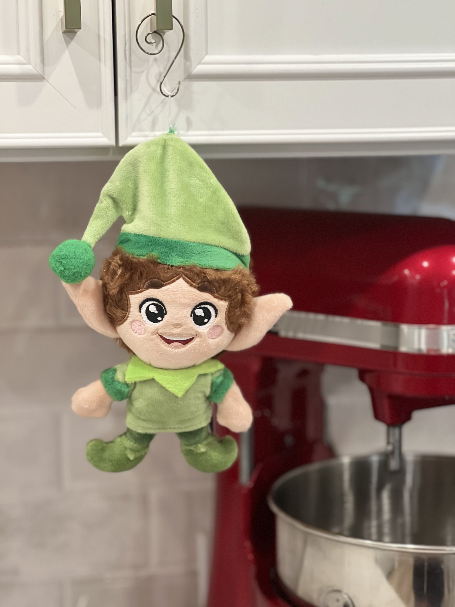Green Kringle Elf hanging on a cabinet hook by a red mixer