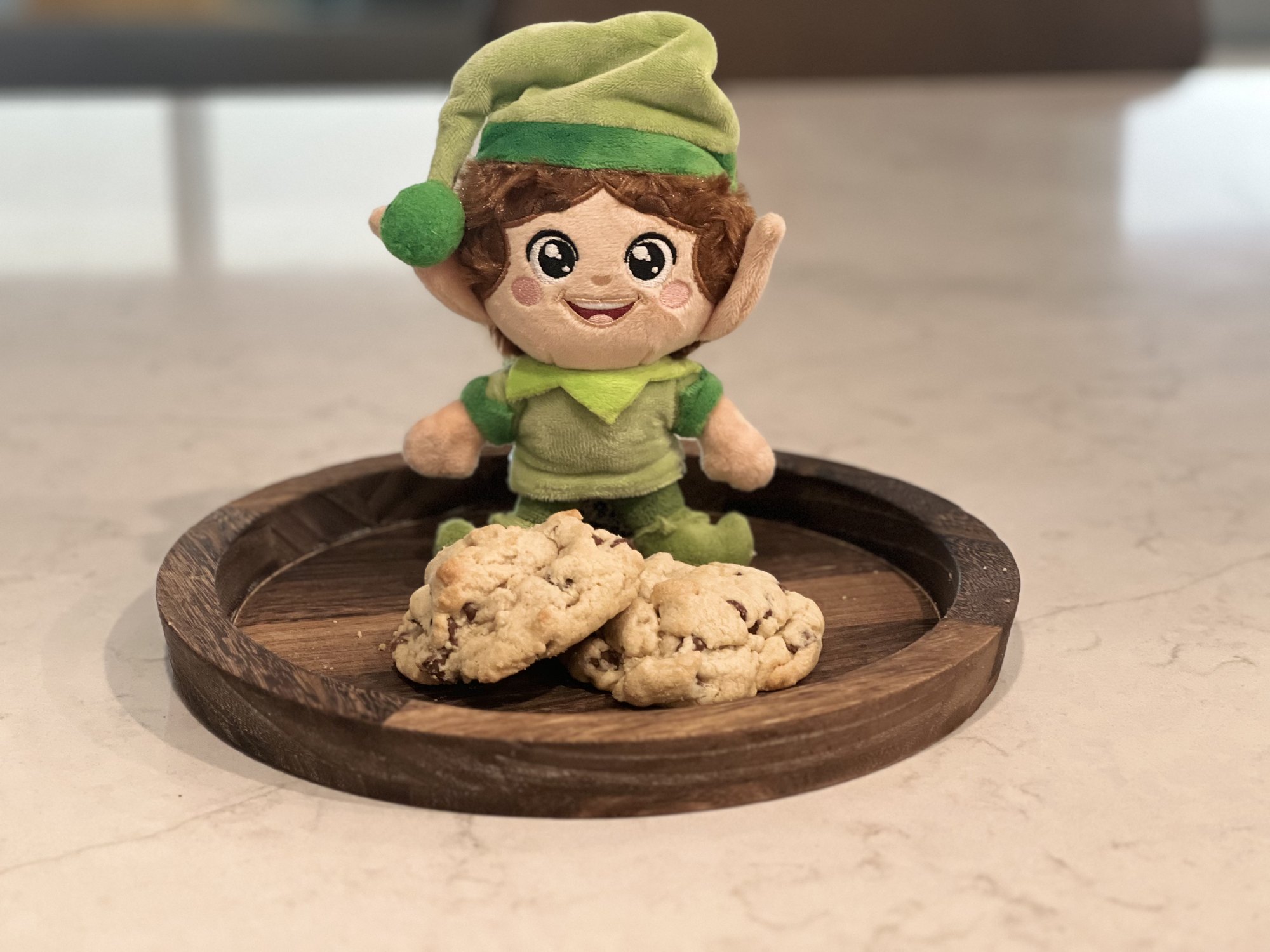 Green Kringle Elf on a wooden tray with two chocolate chip cookies